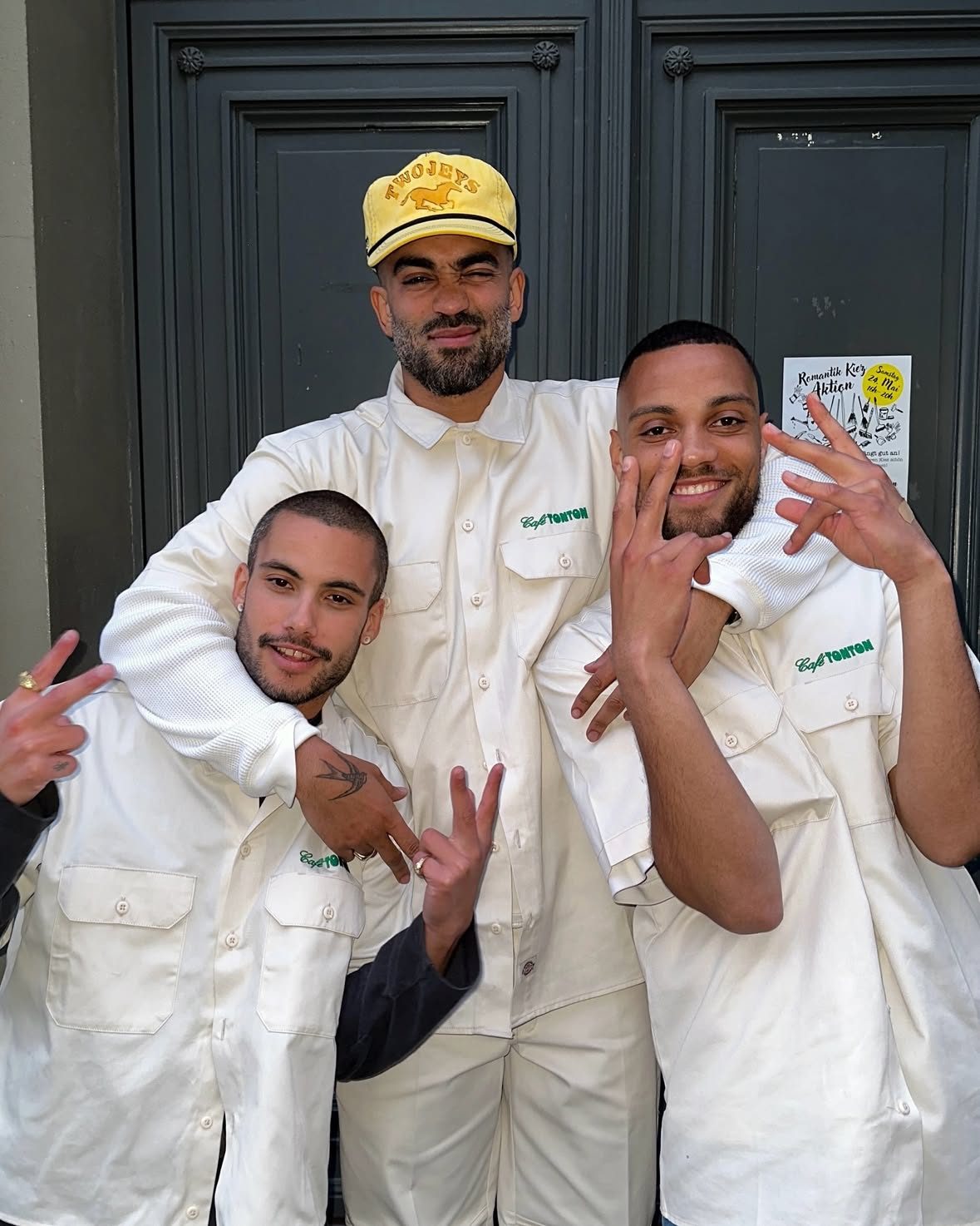 Three Tontons in cream workwear with the green Café TonTon logo