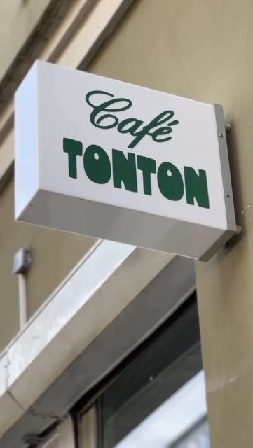 The white hanging box sign with green Café TONTON lettering on the building wall