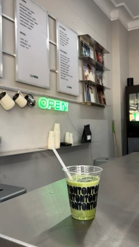 An iced matcha in a TONTON-printed cup on the steel counter, the green OPEN sign behind it