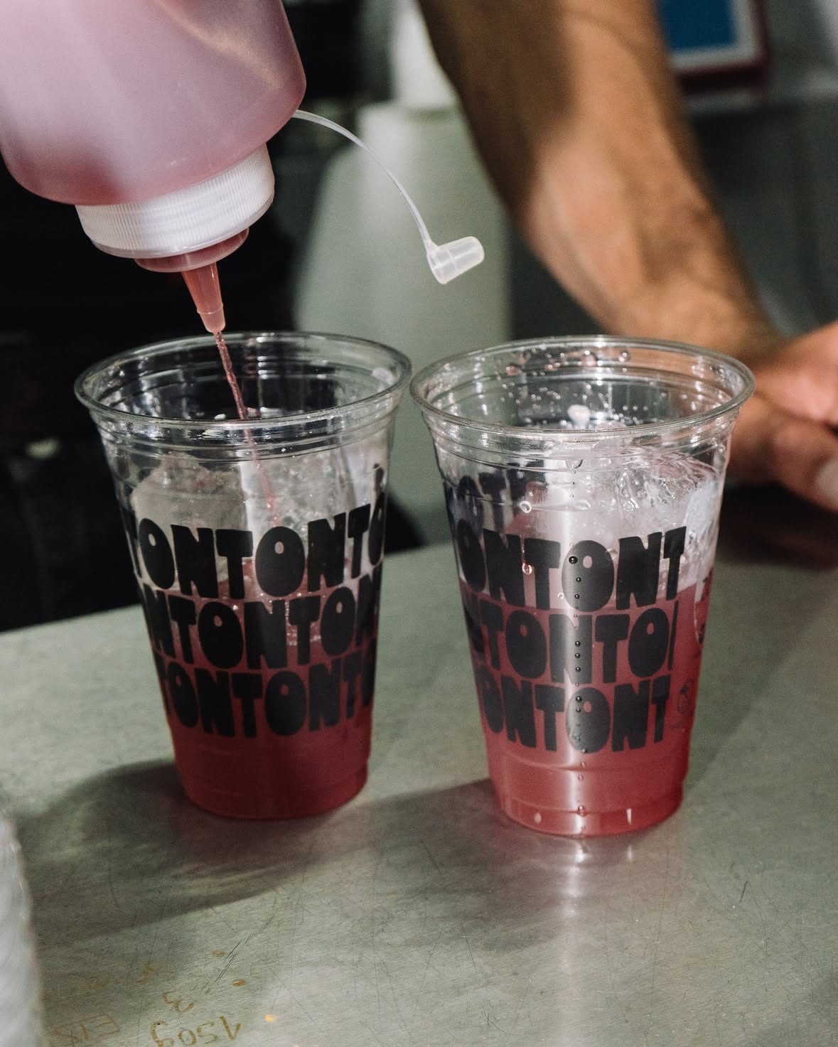 A pink drink poured into two TONTON-printed cups on the steel counter