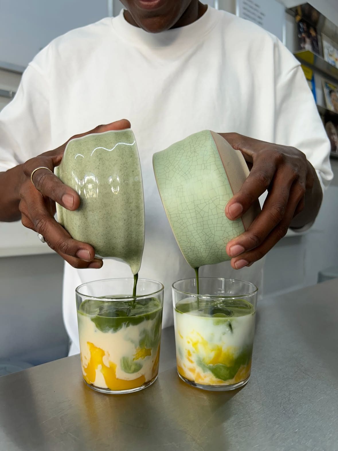 Matcha poured from two ceramic bowls over mango and milk in two glasses