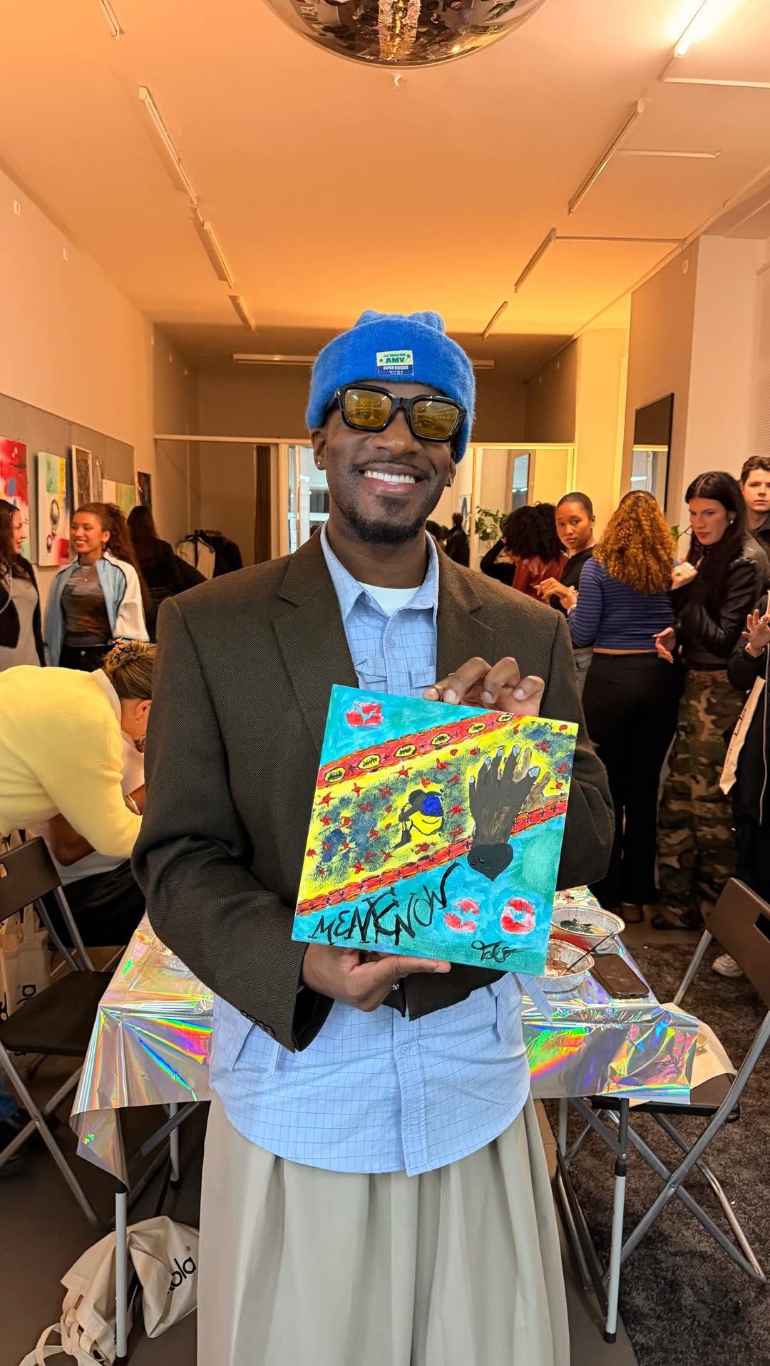A guest in a blue hat holding up a painted canvas at the event